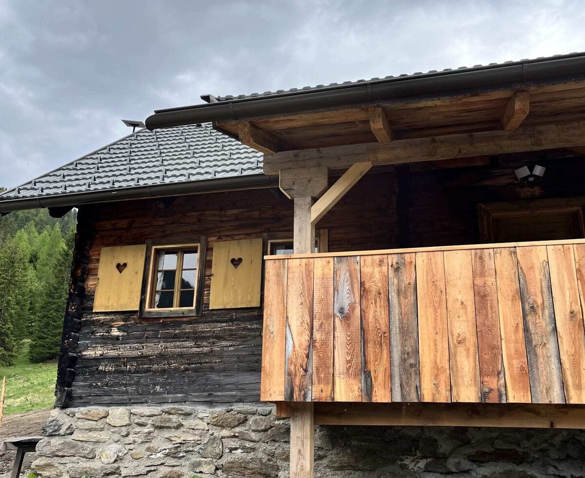 Eine traditionelle hölzerne Alm mit einem rustikalen Balkon, einem Natursteinfundament und charmanten Fensterläden mit Herz-Ausschnitten.