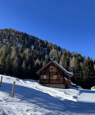 Eine urige Alm inmitten einer verschneiten Winterlandschaft unter strahlend blauem Himmel.