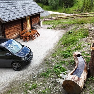 Die urige Alm bietet einen bequemen Parkplatz direkt vor der Tür sowie eine gemütliche Sitzecke und einen rustikalen Holzbrunnen.