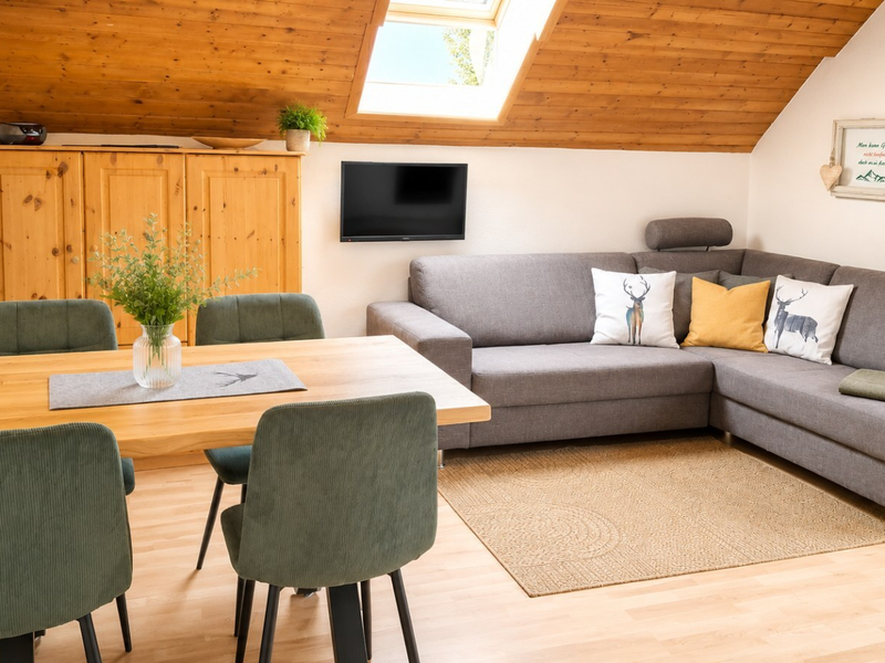 Wohnbereich der Ferienwohnung Alpenblick im Bauernhof mit Esstisch, Ecksofa, Fernseher und Dachfenster.