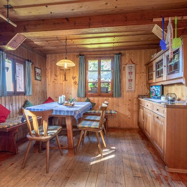Der Essbereich der Alm mit Holztisch, Sitzbank, Stühlen und integrierter Anrichte vor holzvertäfelten Wänden.