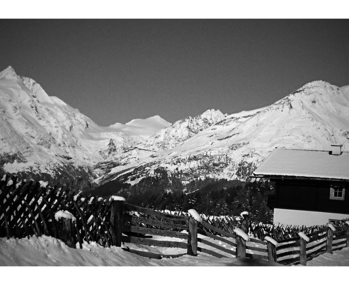 Außenansicht der Almhütte im Schnee mit Blick auf die schneebedeckten Bergspitzen.