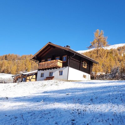 Die Almhütte in der verschneiten Landschaft im goldenen Lärchenwald.