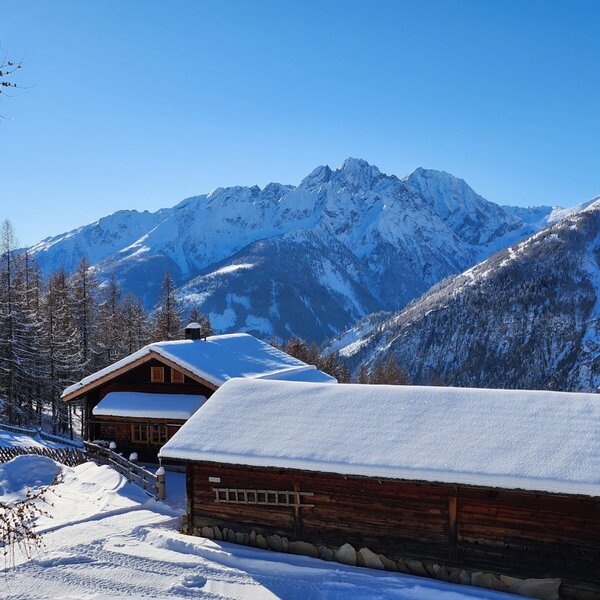 Die verschneite Almhütte, umgeben von einer Winterlandschaft mit schneebedeckten Bergen.