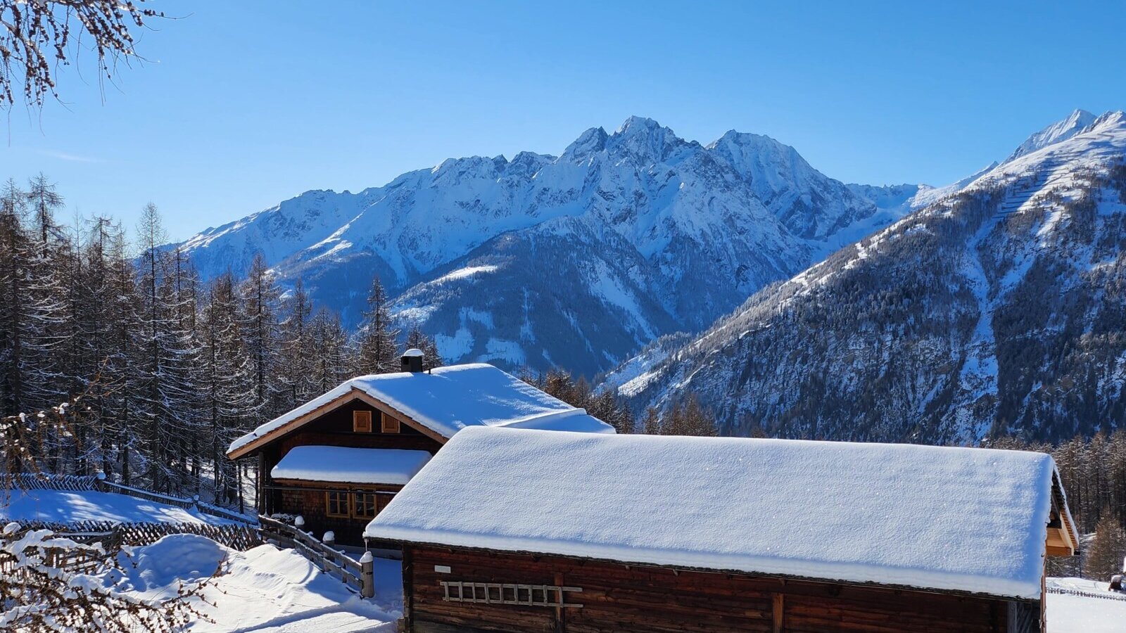 Die verschneite Almhütte, umgeben von einer Winterlandschaft mit schneebedeckten Bergen.