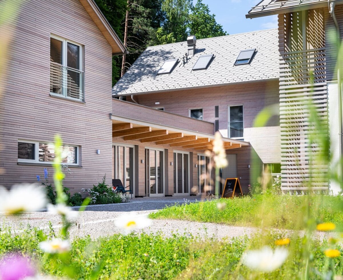 Außenansicht der Ferienwohnung mit moderner Holzfassade und überdachtem Eingangsbereich, umgeben von Grünflächen.