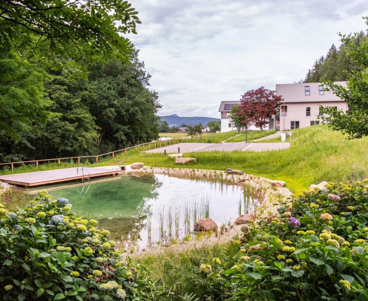 Der Teich des Hauses mit Holzdeck, umgeben von Grünflächen und Blumen.