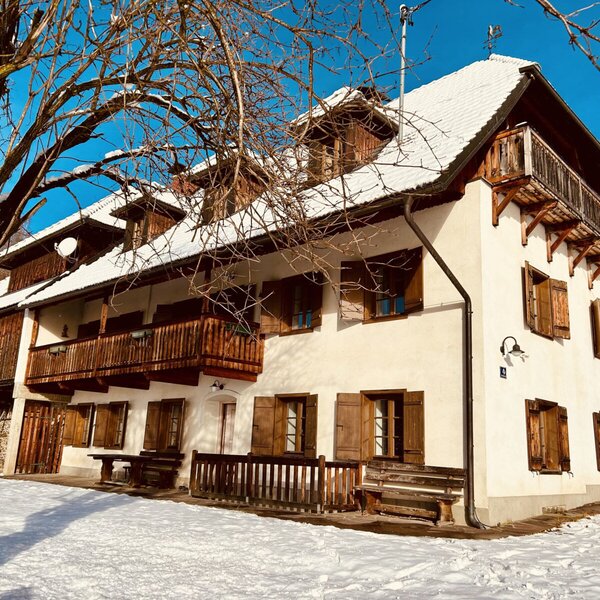 Außenansicht des Ferienhauses im Winter, mit Schnee auf dem Dach und den Holzbalkonen sowie Sitzbänken im Freien.