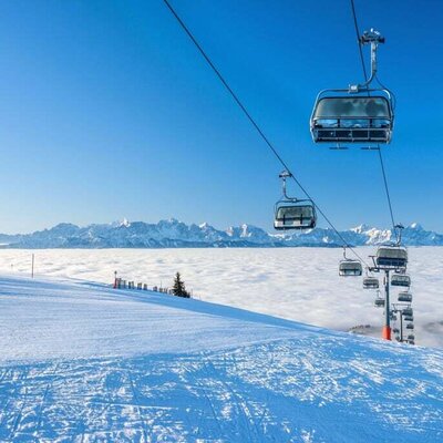 Skipiste auf der Gerlitzen Alpe mit Sesselbahn und Blick über ein Wolkenmeer auf die umliegenden Berge.