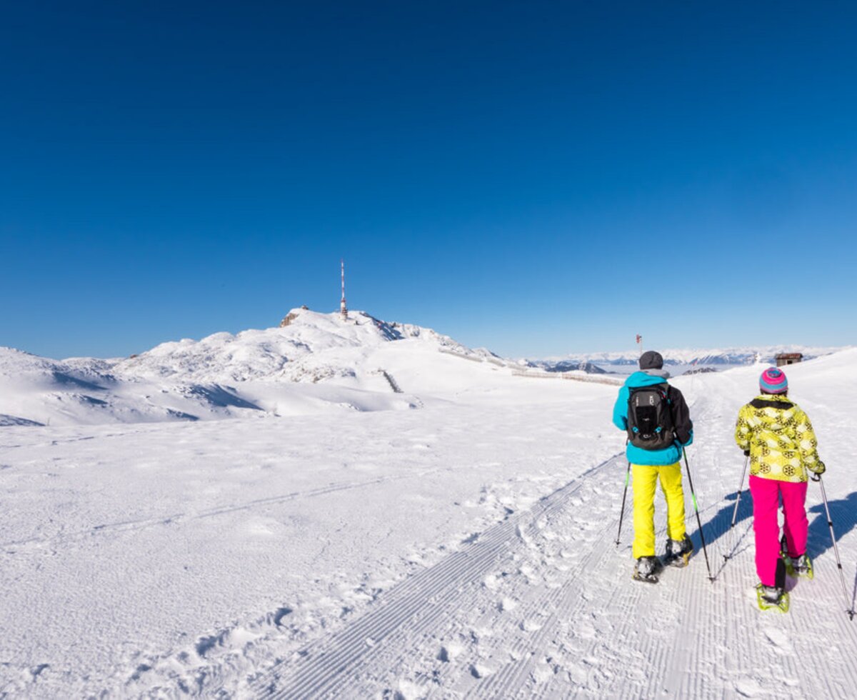 Zwei Personen beim Schneeschuhwandern auf einem präparierten Weg in der verschneiten Berglandschaft der Gerlitzen Alpe.