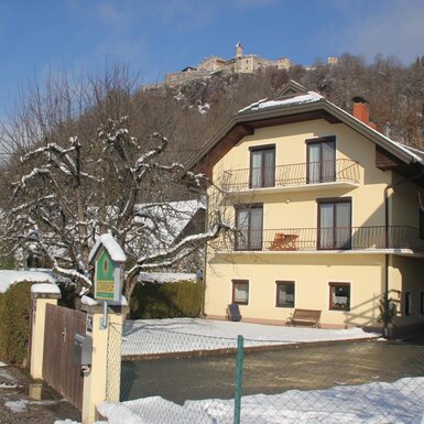 Der Bauernhof SonnHOF mit seinen Ferienwohnungen im Winter, inklusive Balkonen und Blick auf die Burgruine Landskron.