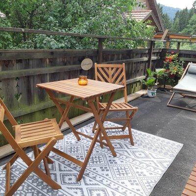 Terrasse des Bauernhofs mit Holztisch, Stühlen und Sonnenliege.