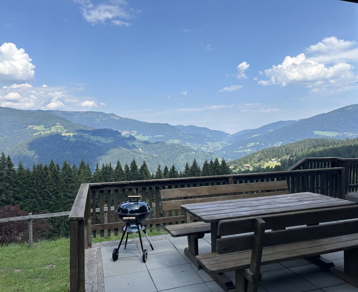 Die einladende Terrasse des Almhauses mit rustikalen Holzmöbeln und einem Grill bietet einen weiten Ausblick auf die grünen Nockberge.
