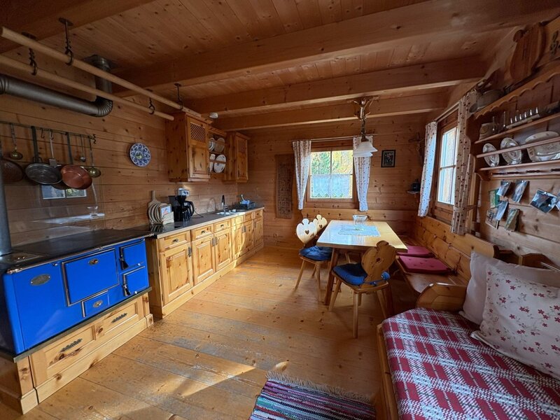 Küche und Essbereich der Alm mit blauem Holzherd, Holzeinrichtung, Esstisch und Eckbank.