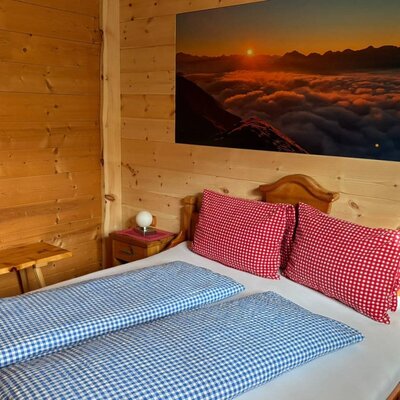 Schlafzimmer in der Alm mit Holzwänden, einem Doppelbett, einem Nachttisch und einem Wandbild mit Bergszene.