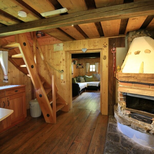 Die Wohnküche der Almhütte mit Küchenzeile, Holztreppe zum Obergeschoss und einem großen Kaminofen.