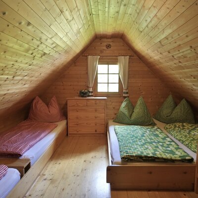 Schlafstube in der Alm mit vier Einzelbetten, Holzwänden, einem Fenster und einer Kommode.