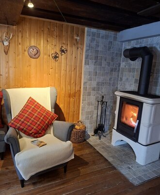 Eine gemütliche Ecke in der Hütte mit einem einladenden Sessel und einem wärmenden Kaminofen.