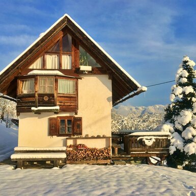 Die Alm im Winter, mit verschneitem Erker, Holzbalkon und gestapeltem Brennholz.