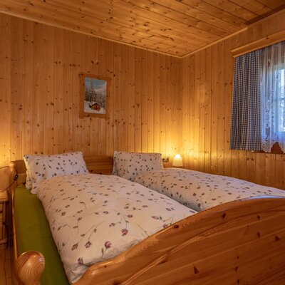 Schlafzimmer in der Alm mit zwei Einzelbetten, Holzwänden, Nachttisch und Fenster.