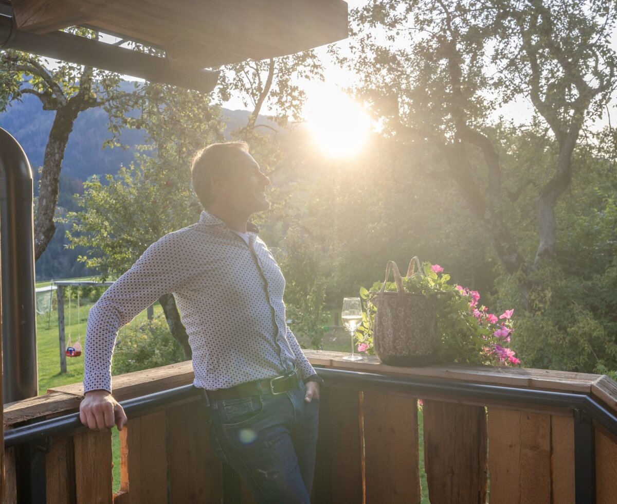 Die Holzterrasse des Ferienhauses mit einem Getränk und Blick auf die umliegende Natur im Sonnenschein.