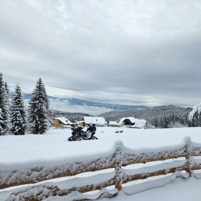 Verschneite Winterlandschaft der Alm mit einem Holzzaun und Blick auf das Jauntal.