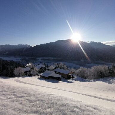 Die verschneite Winterlandschaft rund um den Bauernhof mit Blick auf das Drautal und die umliegenden Berge bei Sonnenschein.
