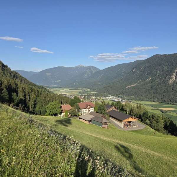 Die idyllische Lage des Bauernhofs an einem saftig grünen Hang mit weitem Ausblick auf das Tal und die umliegenden Berge.