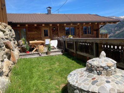 Chalet mit einer Holzterrasse, ausgestattet mit Tisch und Stühlen, umgeben von einer grünen Wiese und Bergblick.