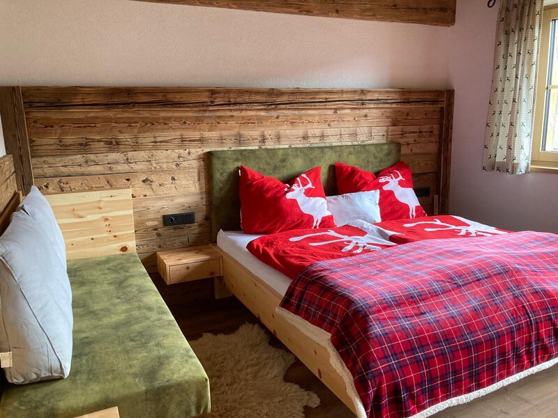 Schlafzimmer in der Alm mit Doppelbett, Holzwandverkleidung und einer grünen Sitzbank.