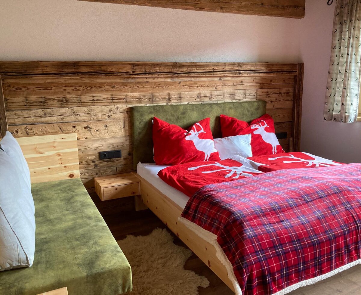 Schlafzimmer in der Alm mit Doppelbett, Holzwandverkleidung und einer grünen Sitzbank.