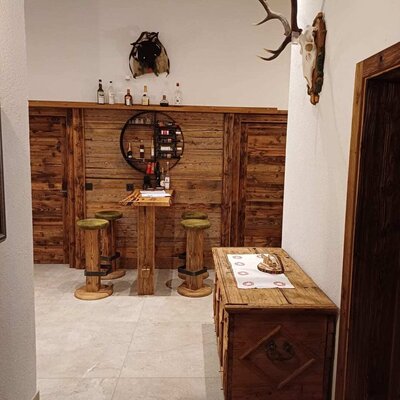 Der Barbereich der Alm, ausgestattet mit Holzelementen, Barhockern und einer Auswahl an Getränken, dekoriert mit einem Hirschgeweih.