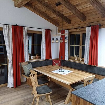 Essbereich der Alm mit großem Holztisch, Eckbank und zwei Stühlen unter einer Decke mit Holzbalken.