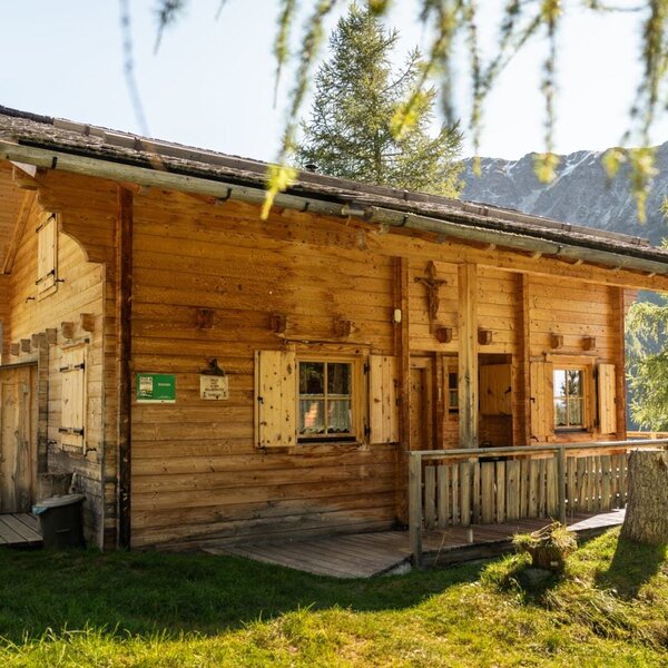 Die Alm von außen, mit Holzfassade, einer kleinen Terrasse und Blick auf die umliegende Berglandschaft.