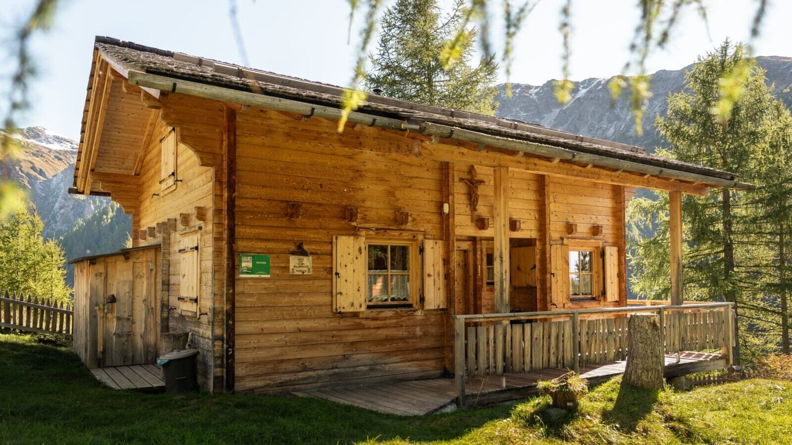 Die Alm von außen, mit Holzfassade, einer kleinen Terrasse und Blick auf die umliegende Berglandschaft.