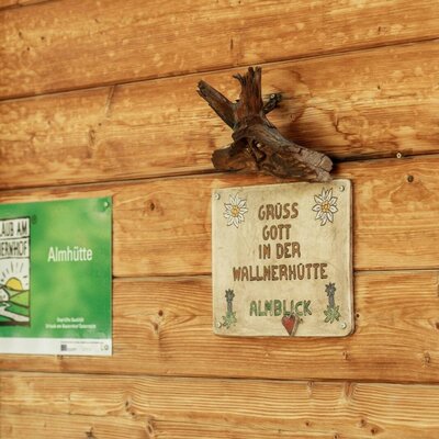 Willkommensschild an der Holzblockwand der Almhütte.
