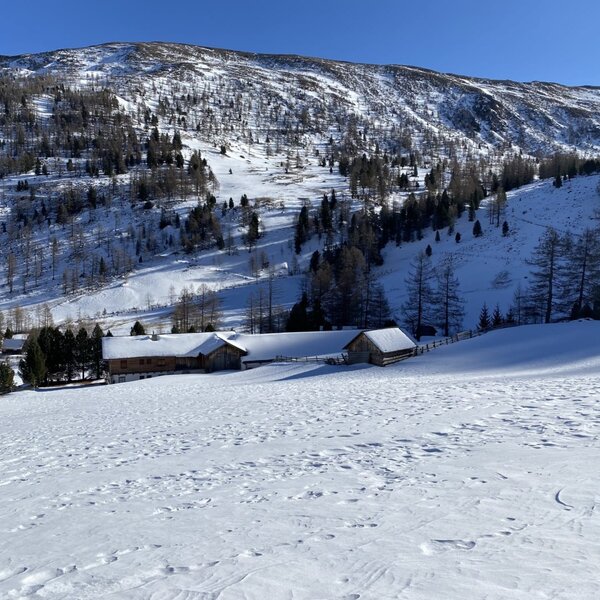 Die Alm in einer verschneiten Winterlandschaft mit Blick auf die Berge des Wolfsbachtals.