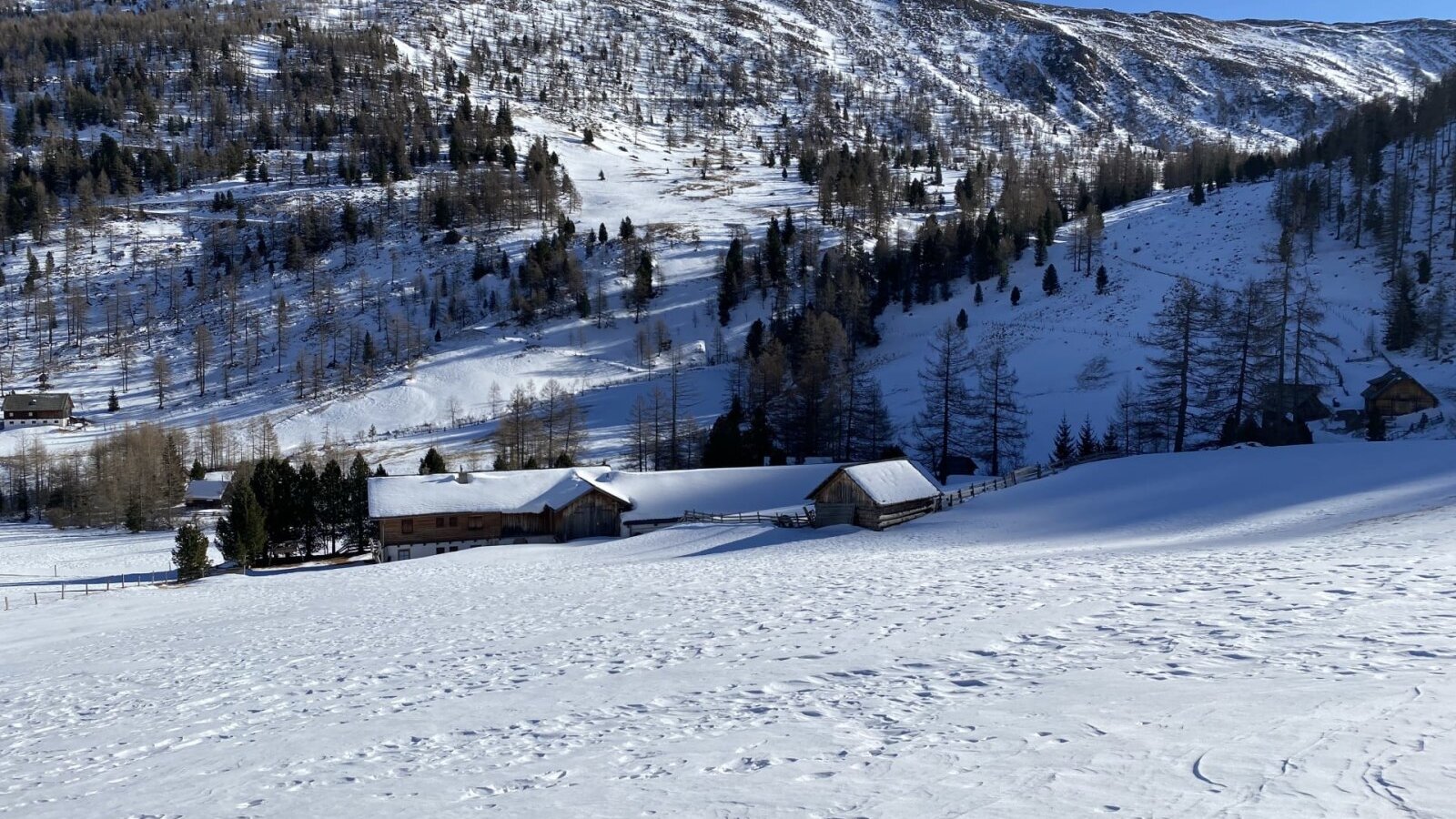 Die Alm in einer verschneiten Winterlandschaft mit Blick auf die Berge des Wolfsbachtals.
