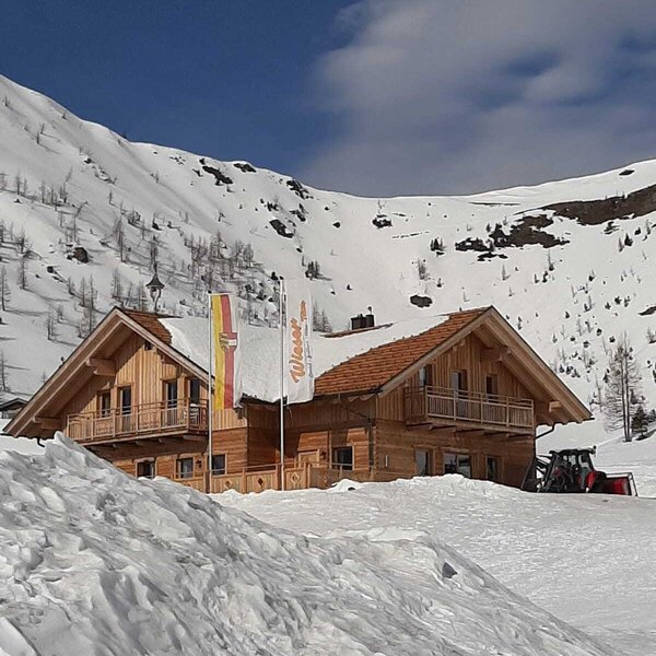 Der Hof als Holzgebäude mit Balkonen in einer verschneiten Berglandschaft.