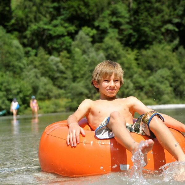 Ein Kind planscht in einem orangefarbenen Schwimmring im Wasser, geeignet für Familienurlaub auf dem Bauernhof.