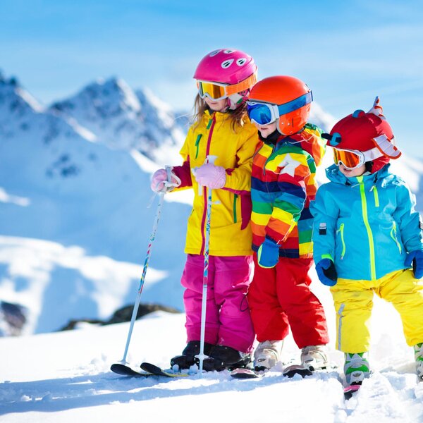 Drei Kinder in bunter Skikleidung beim Wintersport in den Bergen nahe dem Bauernhof.