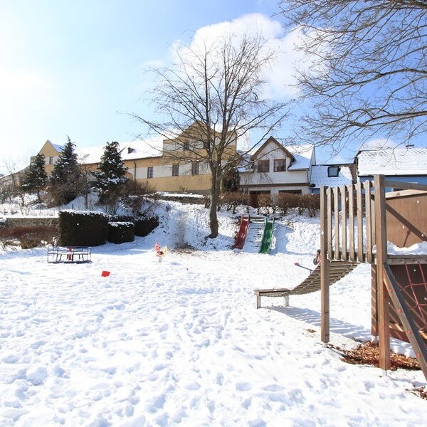 Der schneebedeckte Spielplatz des Bauernhofs mit Rutschen, Schaukeln und einem Klettergerüst.