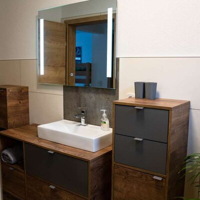 Modernes Badezimmer im Alpakahof mit rechteckigem Waschbecken, beleuchtetem Spiegel und Holzschränken mit dunklen Schubladen.