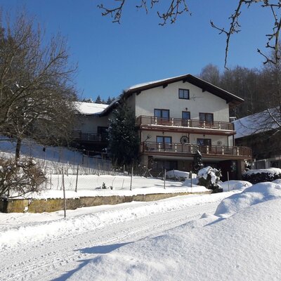 Der Bauernhof von außen im Winter, mit schneebedeckter Umgebung und mehreren Balkonen.