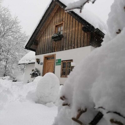 Der schneebedeckte Bauernhof mit traditioneller Holzfassade und weißem Untergeschoss im Winter.