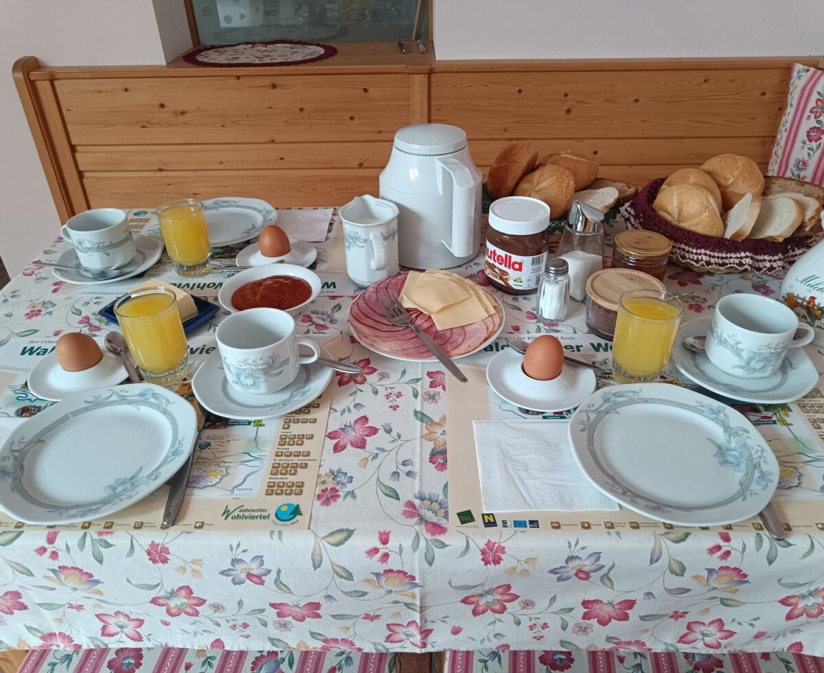 Frühstückstisch im Bauernhof mit Brötchen, Aufschnitt, Käse, Eiern, Saft und Kaffee.