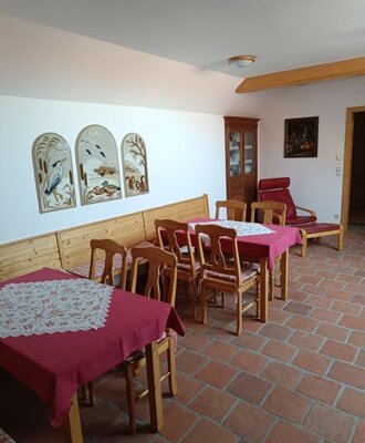Essbereich des Bauernhofs mit Holztischen, Stühlen, Bänken, roten Tischdecken und Terrakottafliesenboden.
