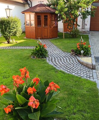 Gartenbereich des Innenhofes mit einer Gartenlaube, einem gepflasterten Weg und blühenden Pflanzen.
