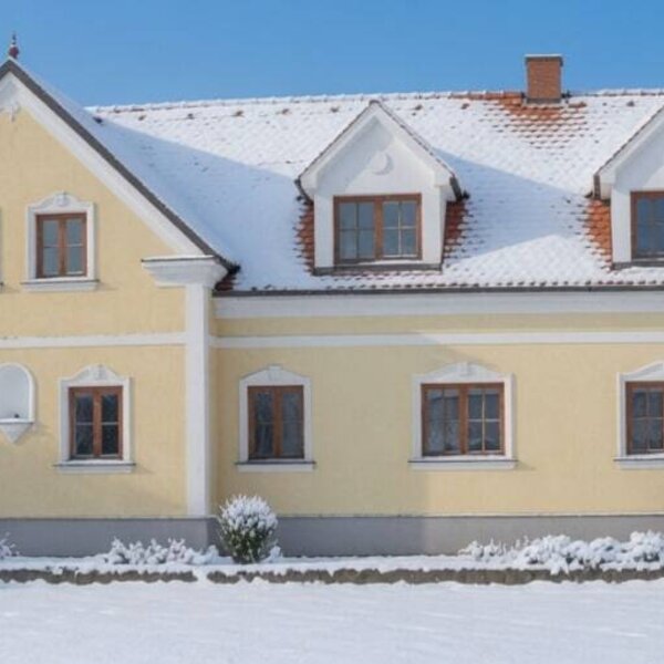 Außenansicht im Winter mit schneebedecktem Dach und gelber Fassade.