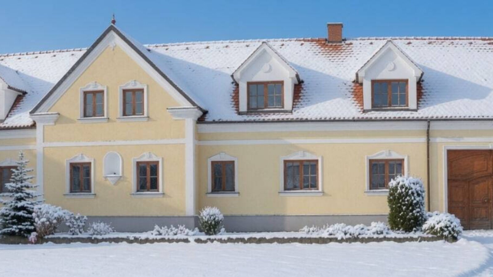 Außenansicht im Winter mit schneebedecktem Dach und gelber Fassade.